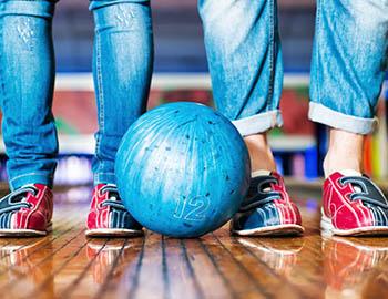 Two pairs of feet with bowling shoes on and a bowling ball