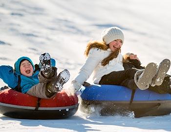 Young kid and sister bombing down the snow tube hill