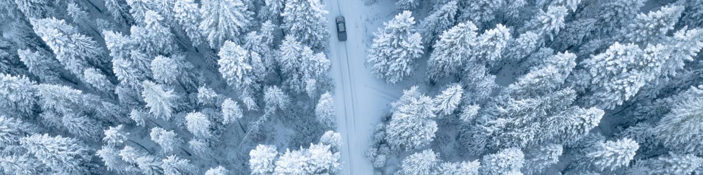 Aerial view of a car driving on a snowy road through a forest