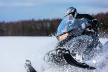 In deep snowdrift snowmobile rider driving fast.