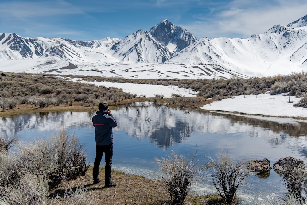 tourist and photographer holding DSLR camera taking photo of Mammoth mountain landscape from the lake