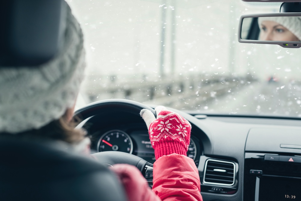 Woman in the red jacket, hat and christmas gloves is driving on the highway at the winter snowfall. View from the back seat of the car.